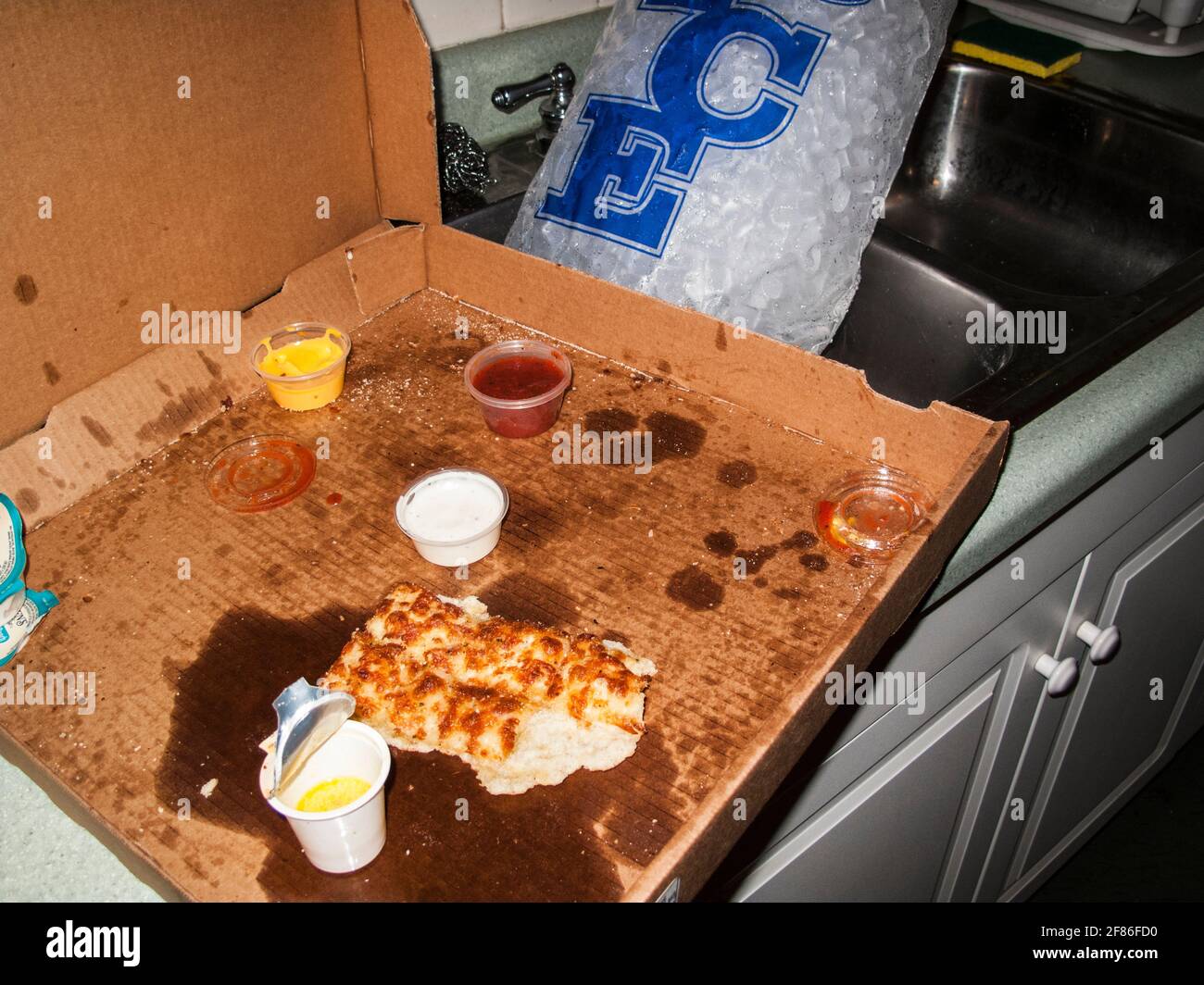 Old half eaten pizza left over after a wild party in a messy house, shot in flash-on-camera style. Stock Photo