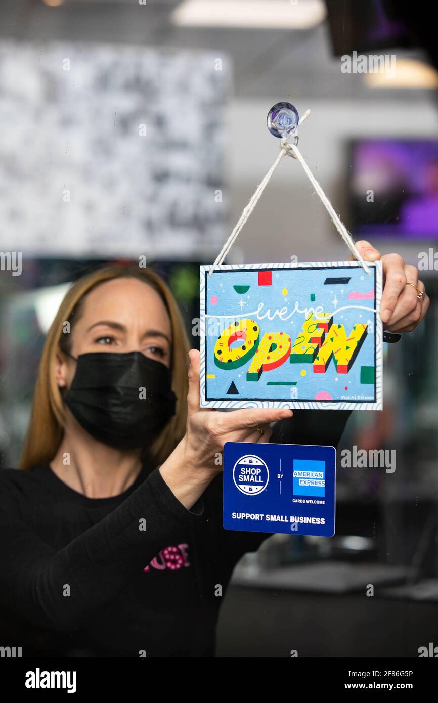 EDITORIAL USE ONLY Manager Louise Hughes from Muse of London displays a 'we're open' sign designed by artist Yukai Du, which has been created as part of the American Express Shop Small campaign and to help welcome people back to our high streets. London. Stock Photo
