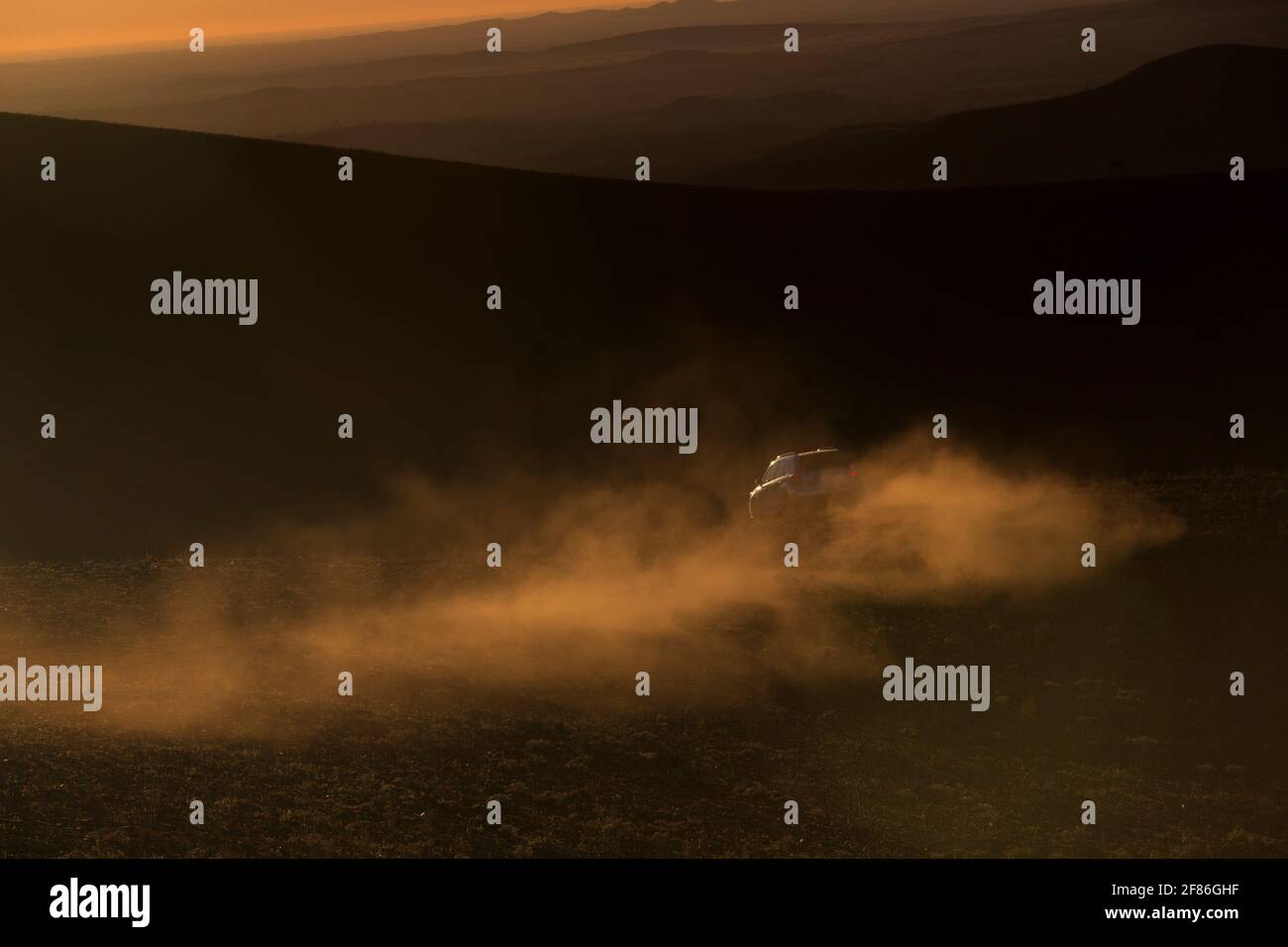 A 4x4 leaves a trail of dust in the sun as it climbs a mountain dirt track. Stock Photo