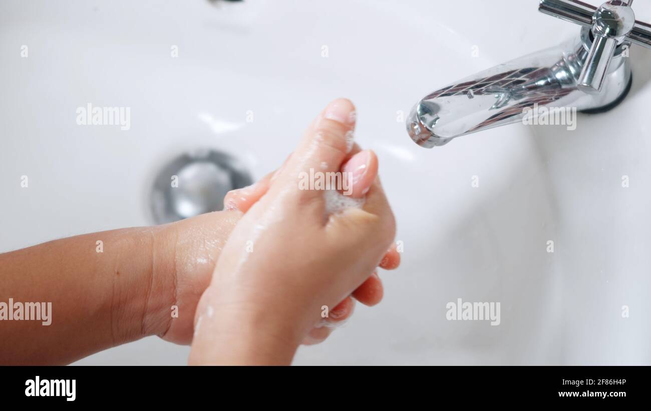 Closeup young woman hands using soap and washing hands under the water ...