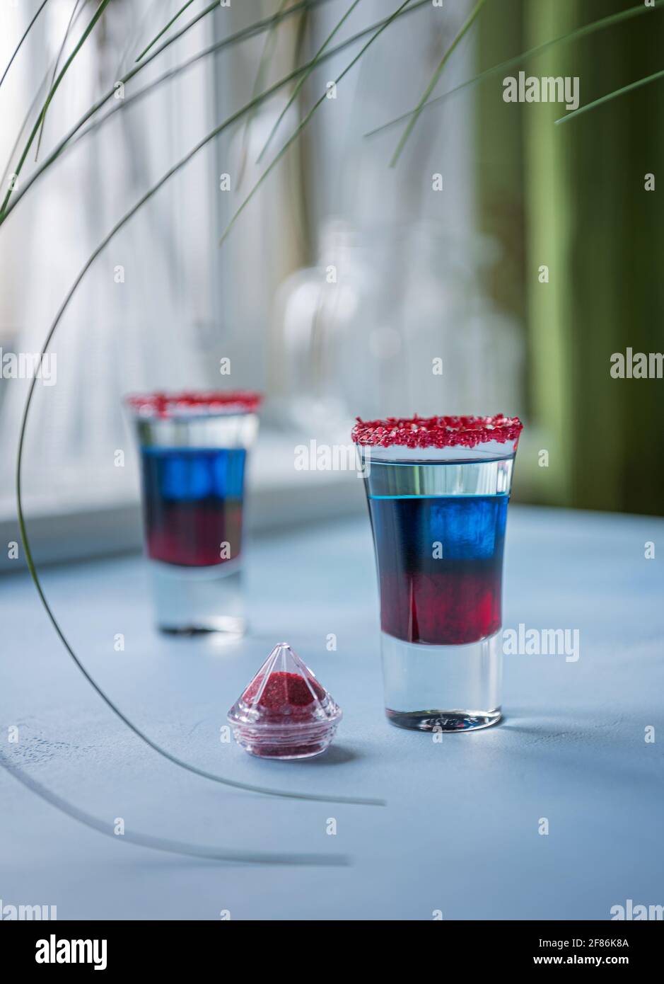 Two shots of Fourth of July alcohol cocktail on blue textured table. Bright red, blue and white layered cocktails in small glasses for USA Independenc Stock Photo