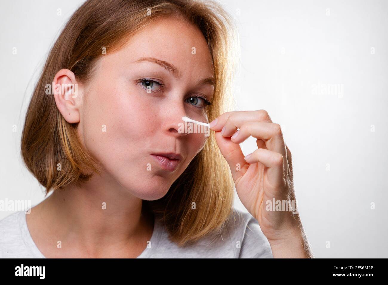 Portrait of a young woman smearing medicine on a pimple on her nose. White background. Acne and pimples concept. Stock Photo