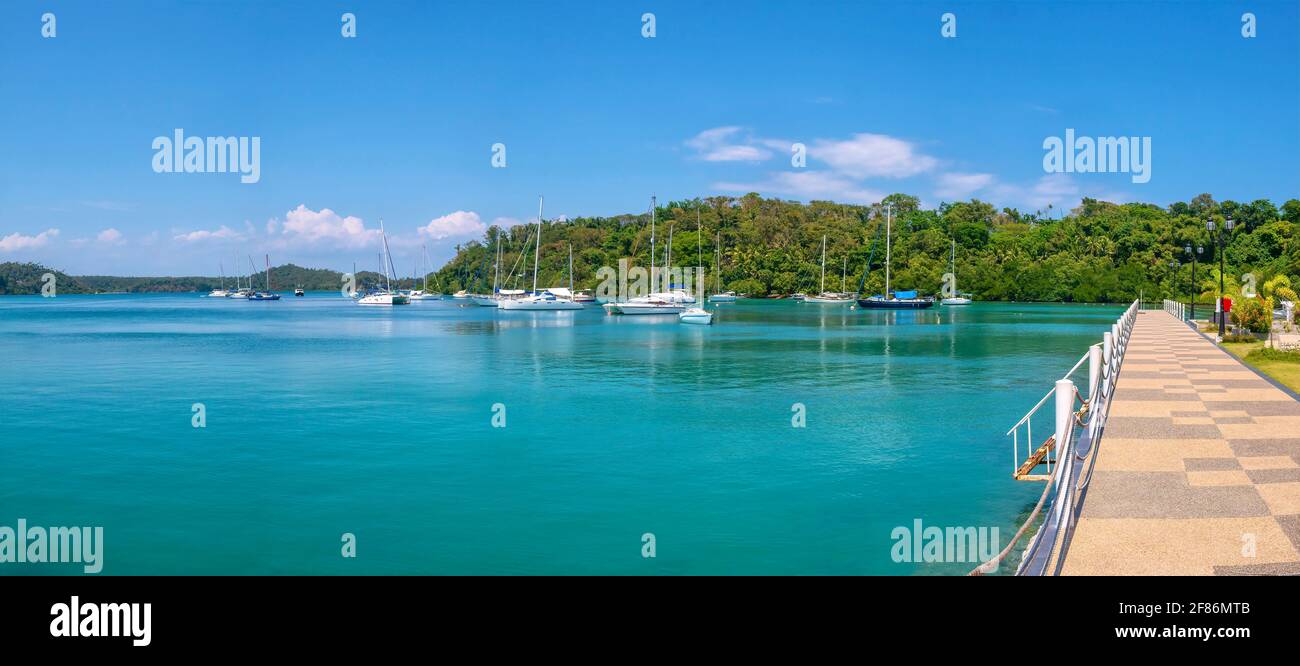 Panoramic view of beautiful Muelle Bay in the tourist resort of Puerto Galera, Philippines, with recreational yachts moored in calm turquoise water. Stock Photo