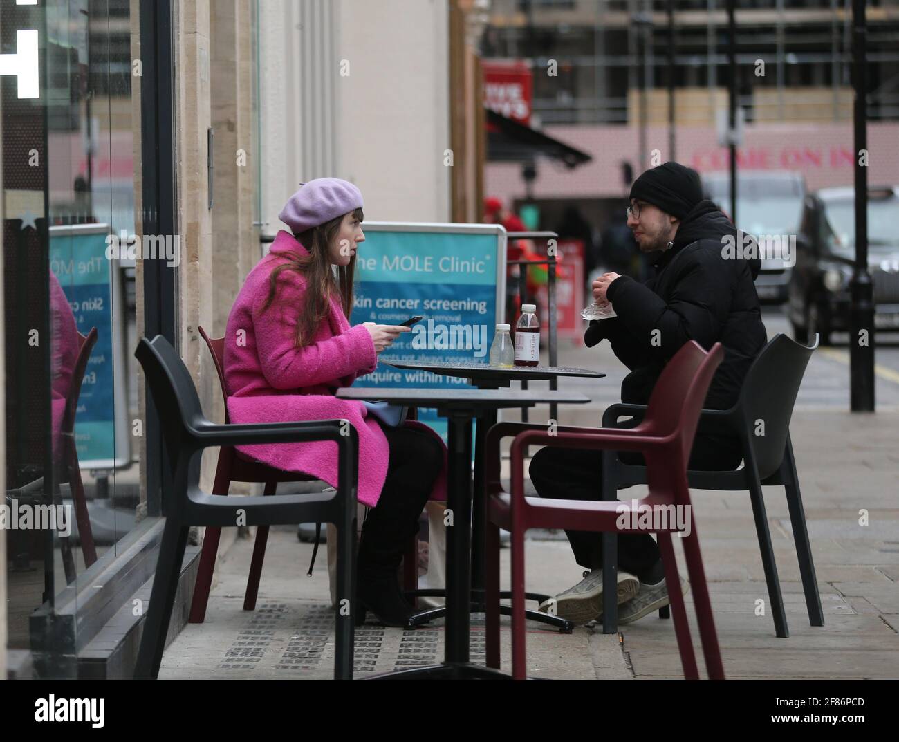 London, England, UK. 12th Apr, 2021. Two people are seen sitting at a table outside a cafe. In a major step in the easing of England's coronavirus lockdown outdoor areas of restaurants, pubs and cafes, all non-essential shops, hairdressers, gyms, swimming pools, nail salons and zoos open today. Credit: Tayfun Salci/ZUMA Wire/Alamy Live News Stock Photo