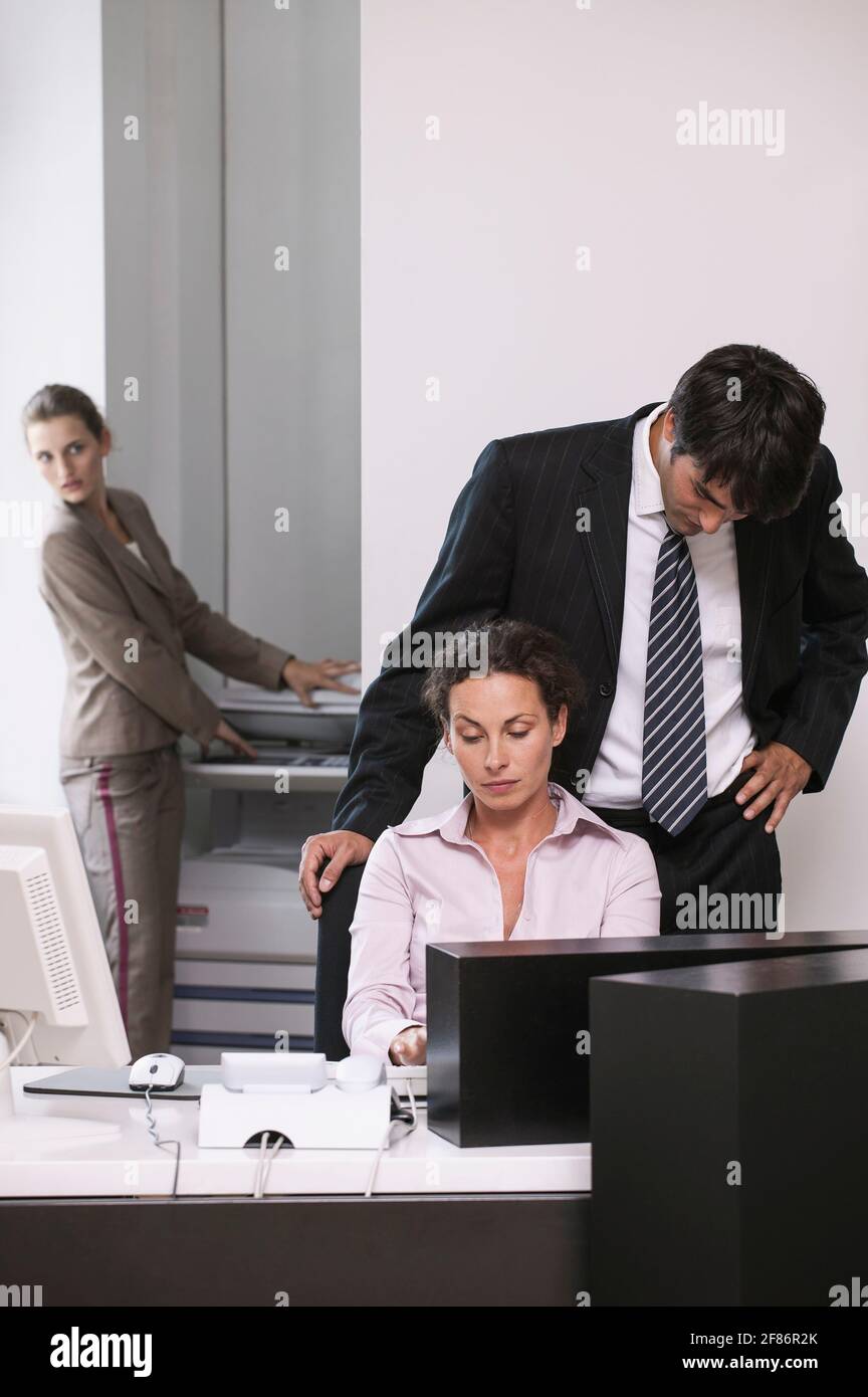 Businessman looking over shoulder of businesswoman in office Stock Photo