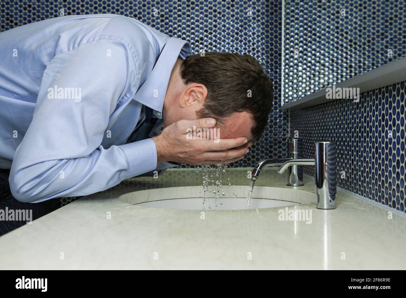 Businessman splashing water on face at bathroom sink Stock Photo