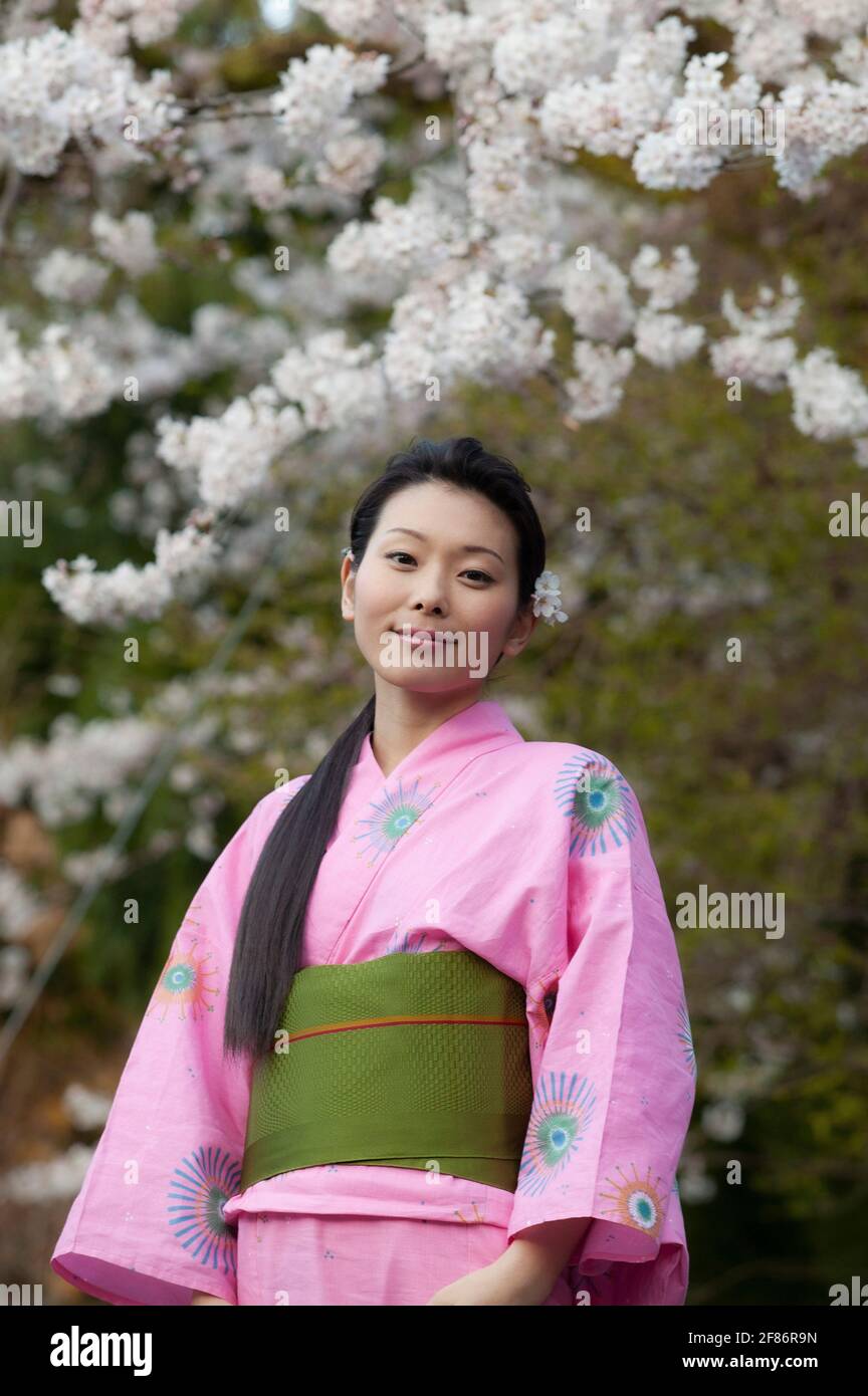 Portrait beautiful young woman in kimono below cherry blossoms Stock Photo