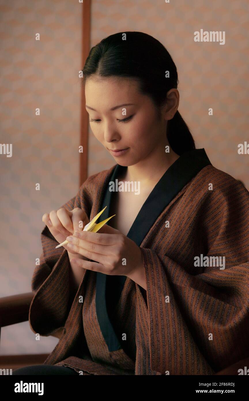 Beautiful young woman in robe making origami paper crane Stock Photo