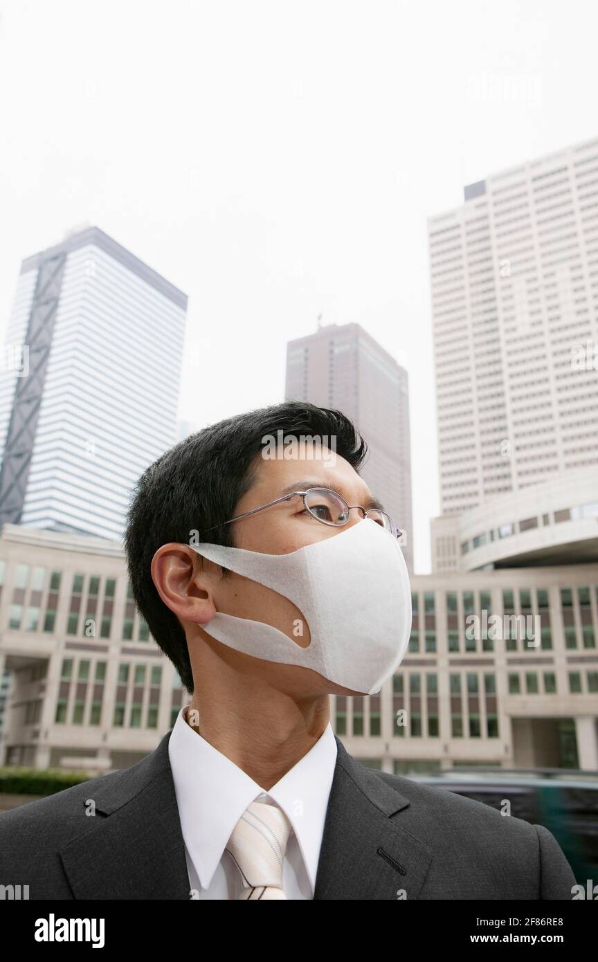 Portrait businessman in face mask below city highrise buildings Stock Photo