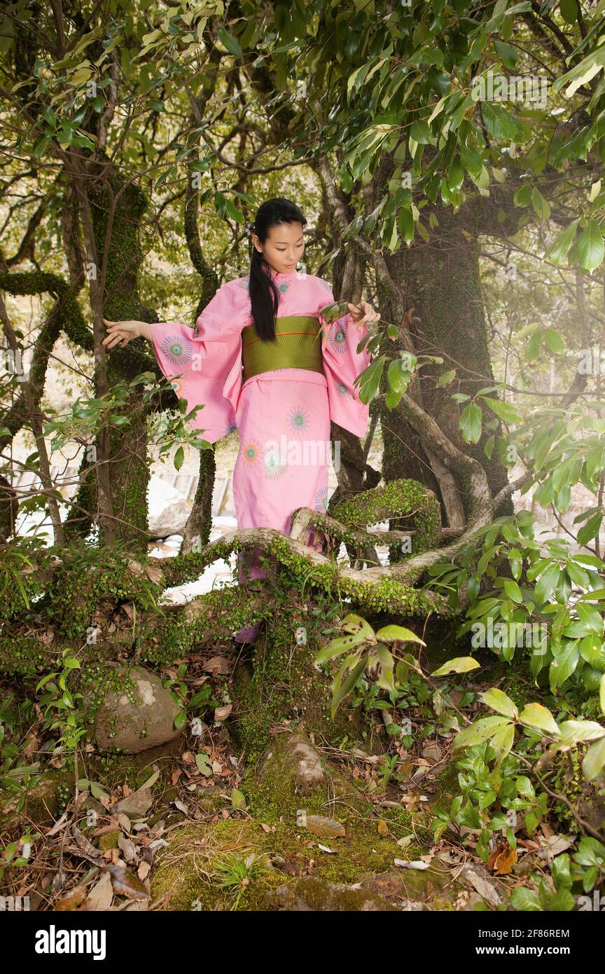 Beautiful young woman in pink kimono below trees Stock Photo