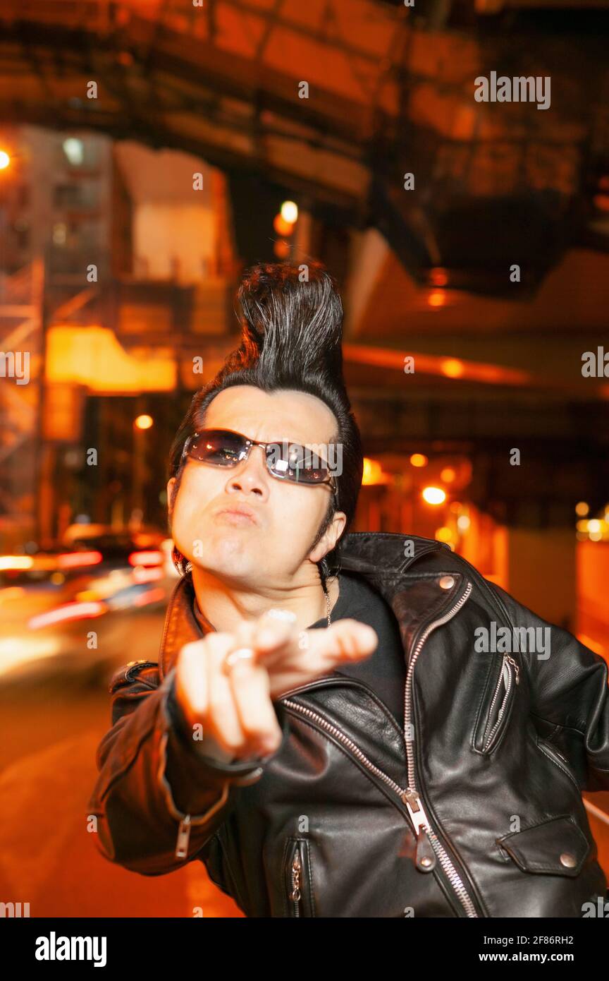 Portrait cool man in sunglasses with mohawk on city street at night Stock Photo