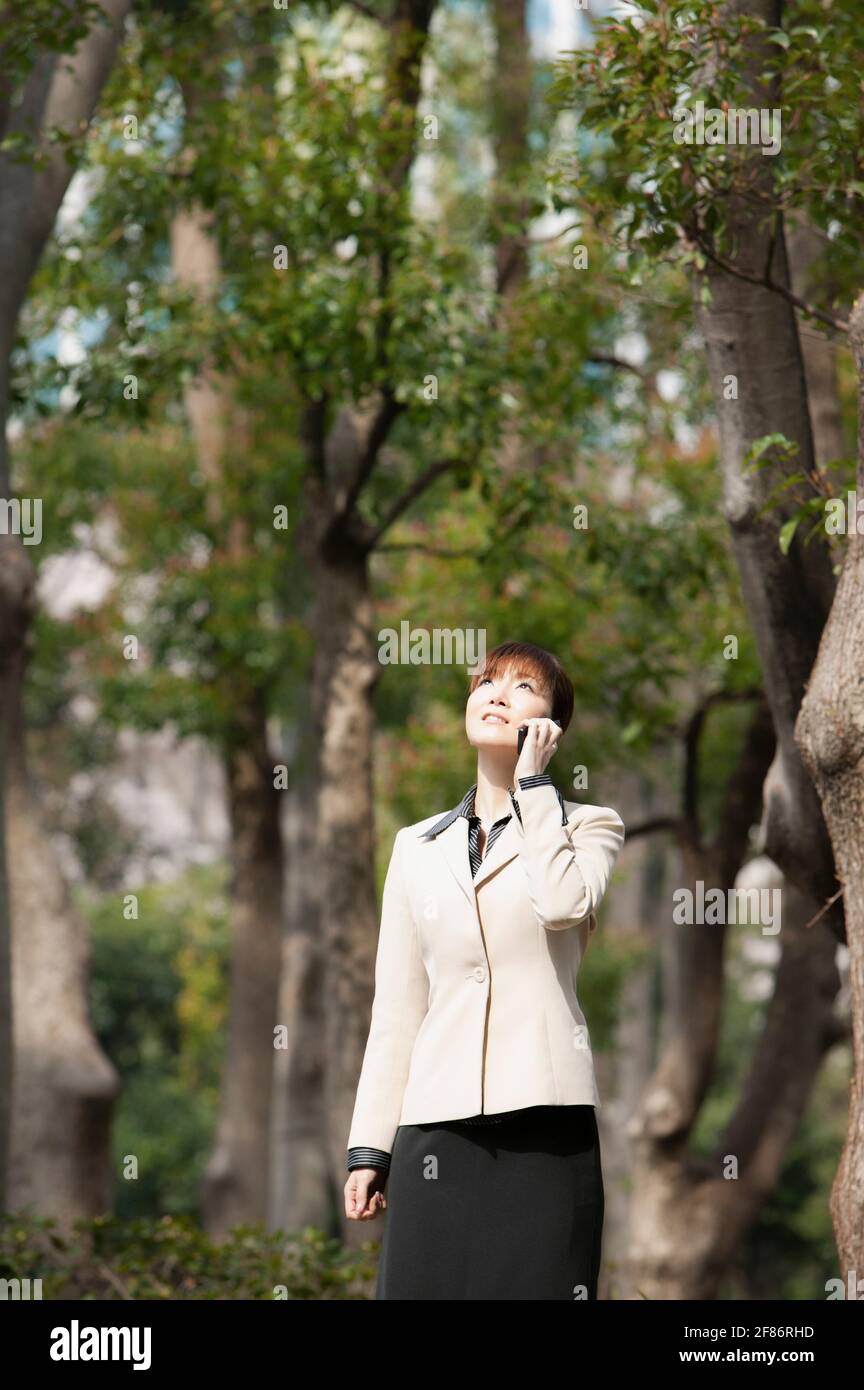 Businesswoman talking on smart phone below trees in park Stock Photo
