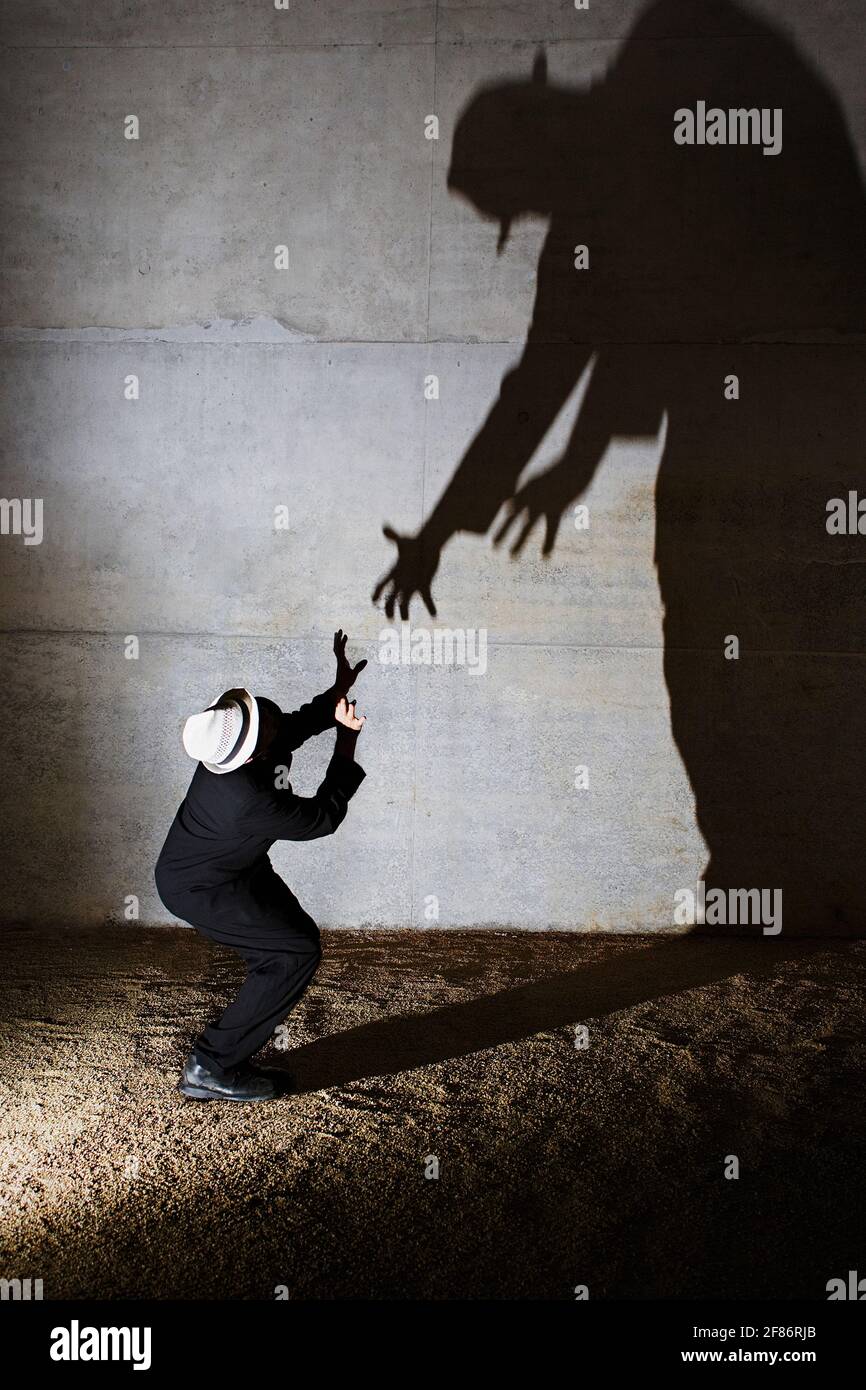 Man cowering from tall ominous shadow on wall Stock Photo
