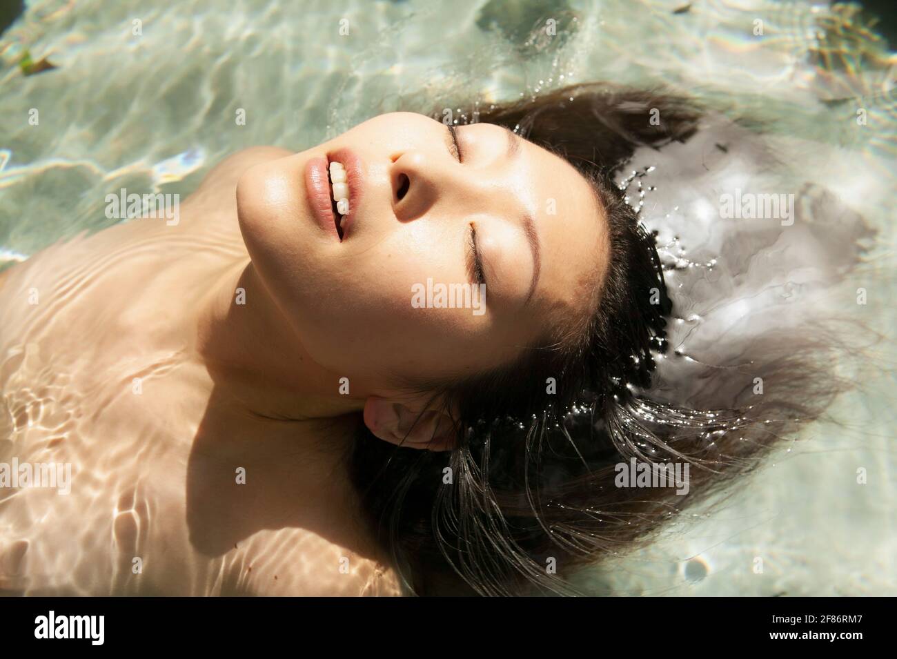 Close up beautiful serene young woman floating in sunny pool Stock Photo