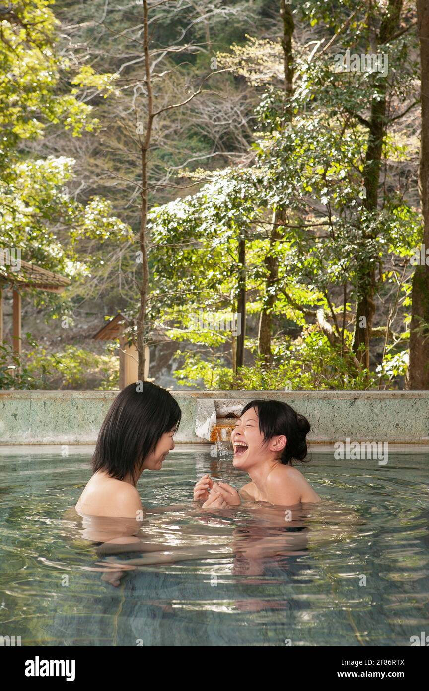 Happy young women friends laughing in soaking pool at Onsen Stock Photo