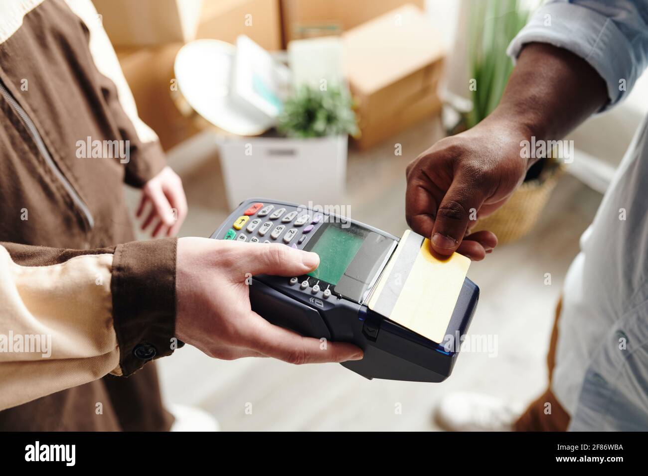 Hand of young man in workwear holding payment terminal while African ...