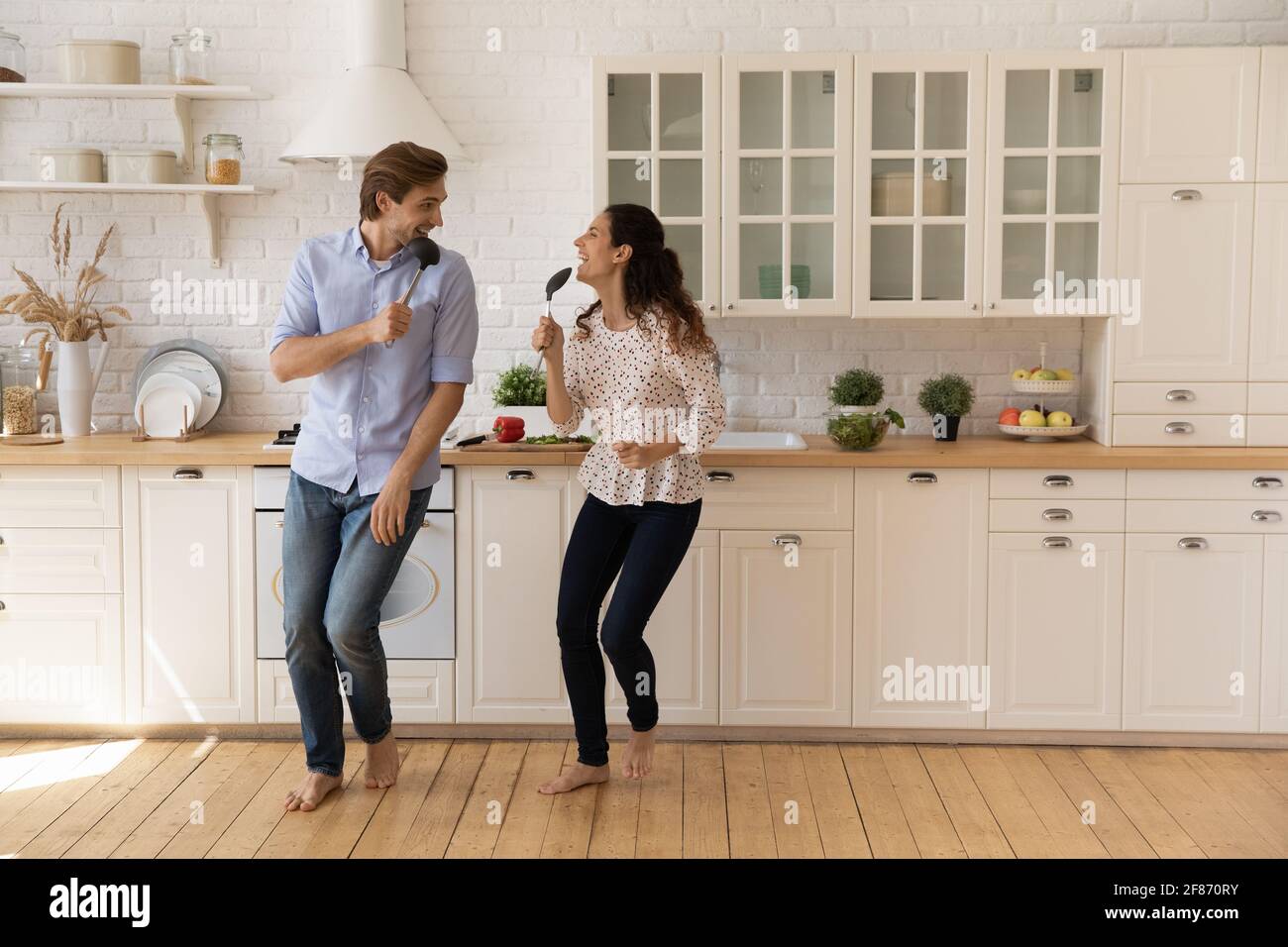 Overjoyed young couple singing into kitchenware, dancing in kitchen Stock Photo