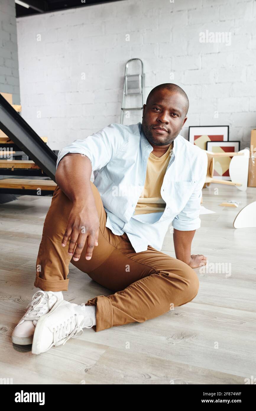 Young African man in brown pants, blue shirt and white cross-shoes sitting  on the floor in front of camera against staircase in living-room Stock  Photo - Alamy