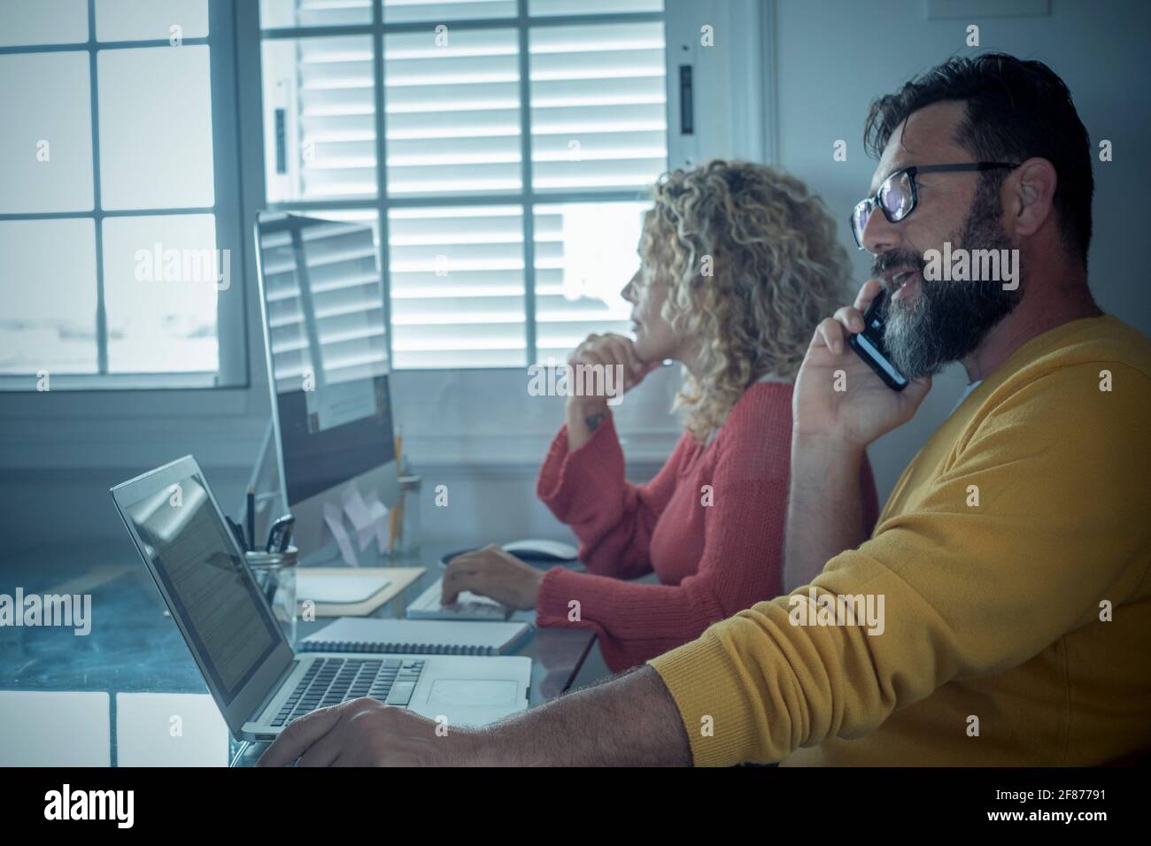 Man and woman team work together in couple at home with technology and online connection laptop computer and phone - smart working and remote workers Stock Photo