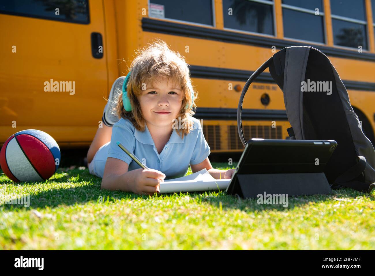 Pupil writing homework on grass with laptop tablet outdoor near school ...
