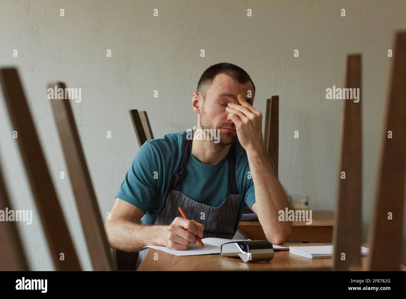 Minimal front view portrait of exhausted young man calculating finances and doing inventory at small business shop, copy space Stock Photo