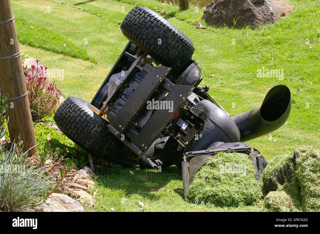 Overturned ride-on lawnmower on steep hillside in private Australian garden. No injuries. Driver jumped clear. Lucky escape, Queensland, Australia. Stock Photo