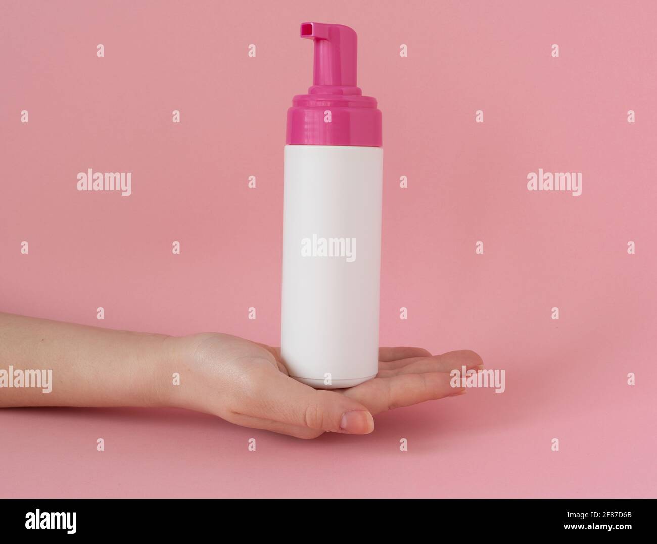 White plastic cosmetic bottle on a woman's hand, face soap, foam, on pink background Stock Photo