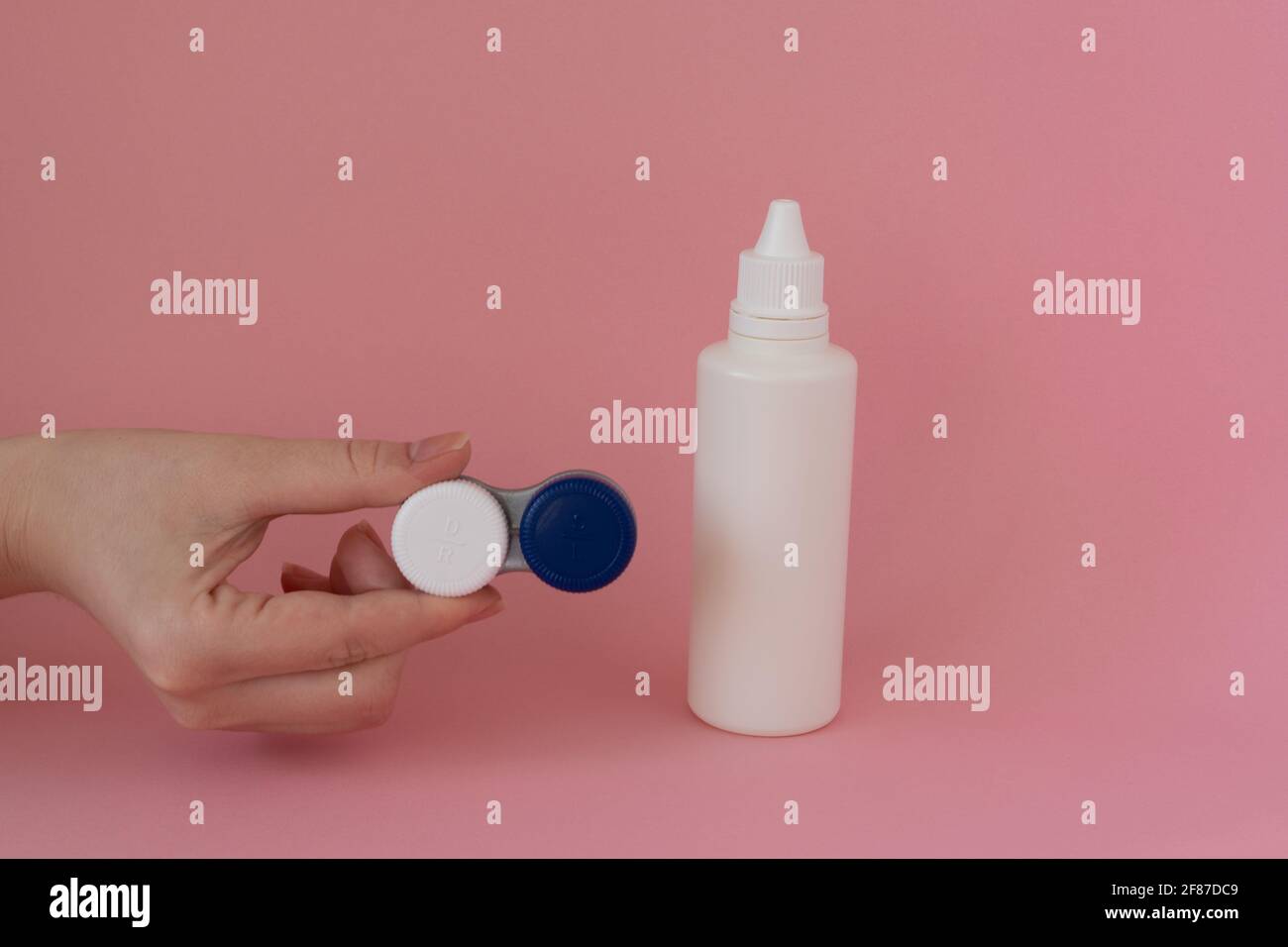 Contact lens case in a woman's hand and bottle of solution on pink background Stock Photo