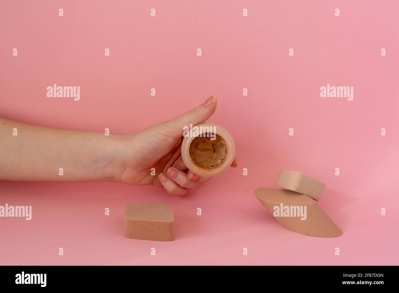 Powder makeup in a woman's hand, sponges for applying face powder on pink background Stock Photo