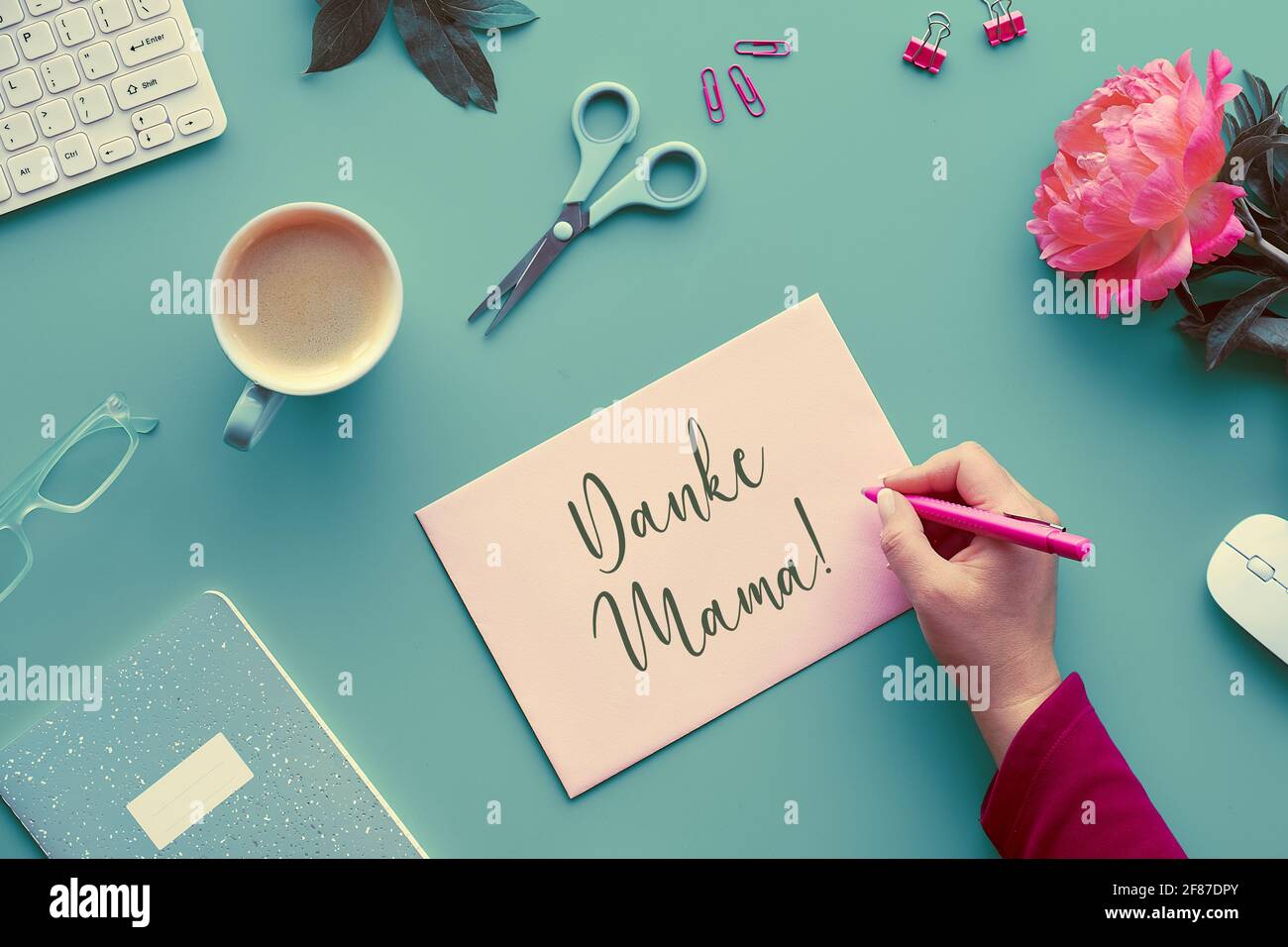 Mothers day greeting card. Text Danke Mama means thank you mom in German. Pink peony flowers on faded mint green table. Coffee, keyboard, flowers Stock Photo