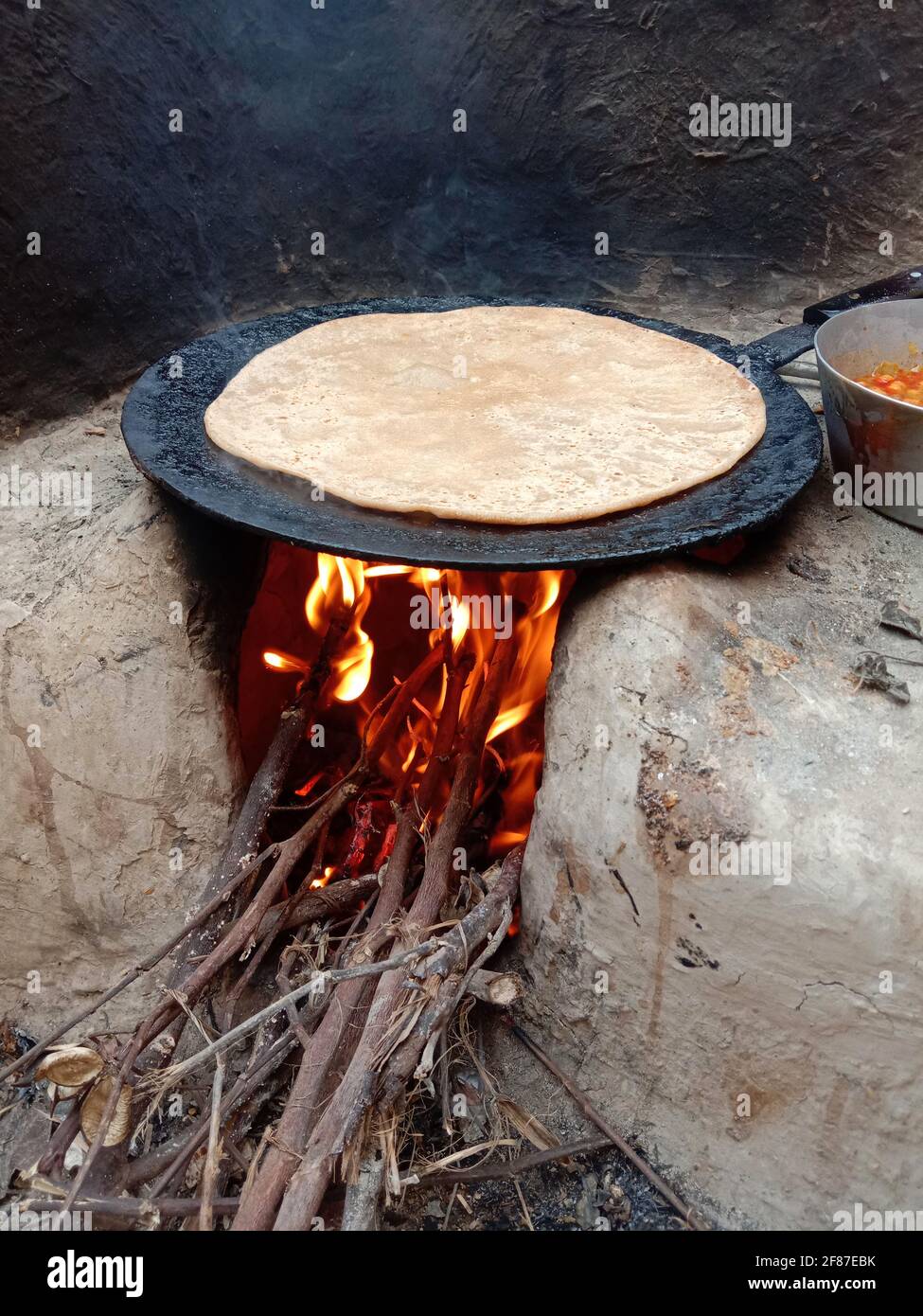 https://c8.alamy.com/comp/2F87EBK/wooden-fire-burning-in-hand-made-mud-stove-with-bread-roti-is-being-baked-on-desi-tawa-village-2F87EBK.jpg