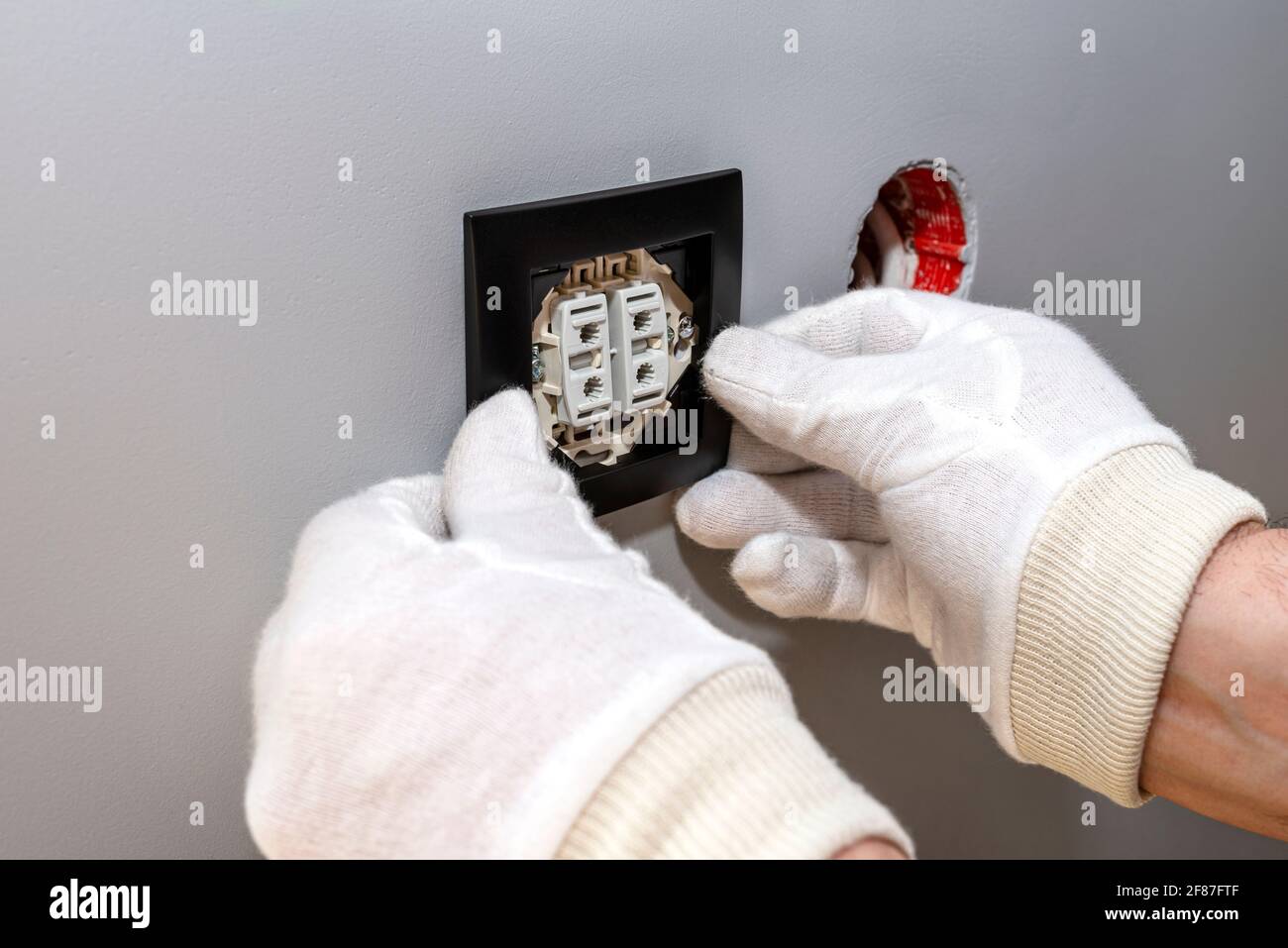 An electrician mounts the black frame of the roller shutter switch up and down with white gloves in the room by the window. Stock Photo