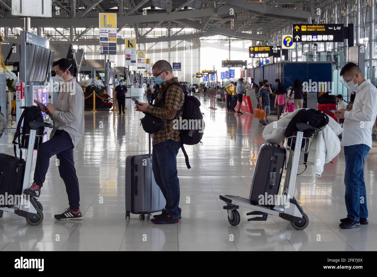 Bangkok, Thailand - April 11, 2021 : asian passengers using smartphones to checking news and waiting in row to check-in for airplane flights in covid- Stock Photo