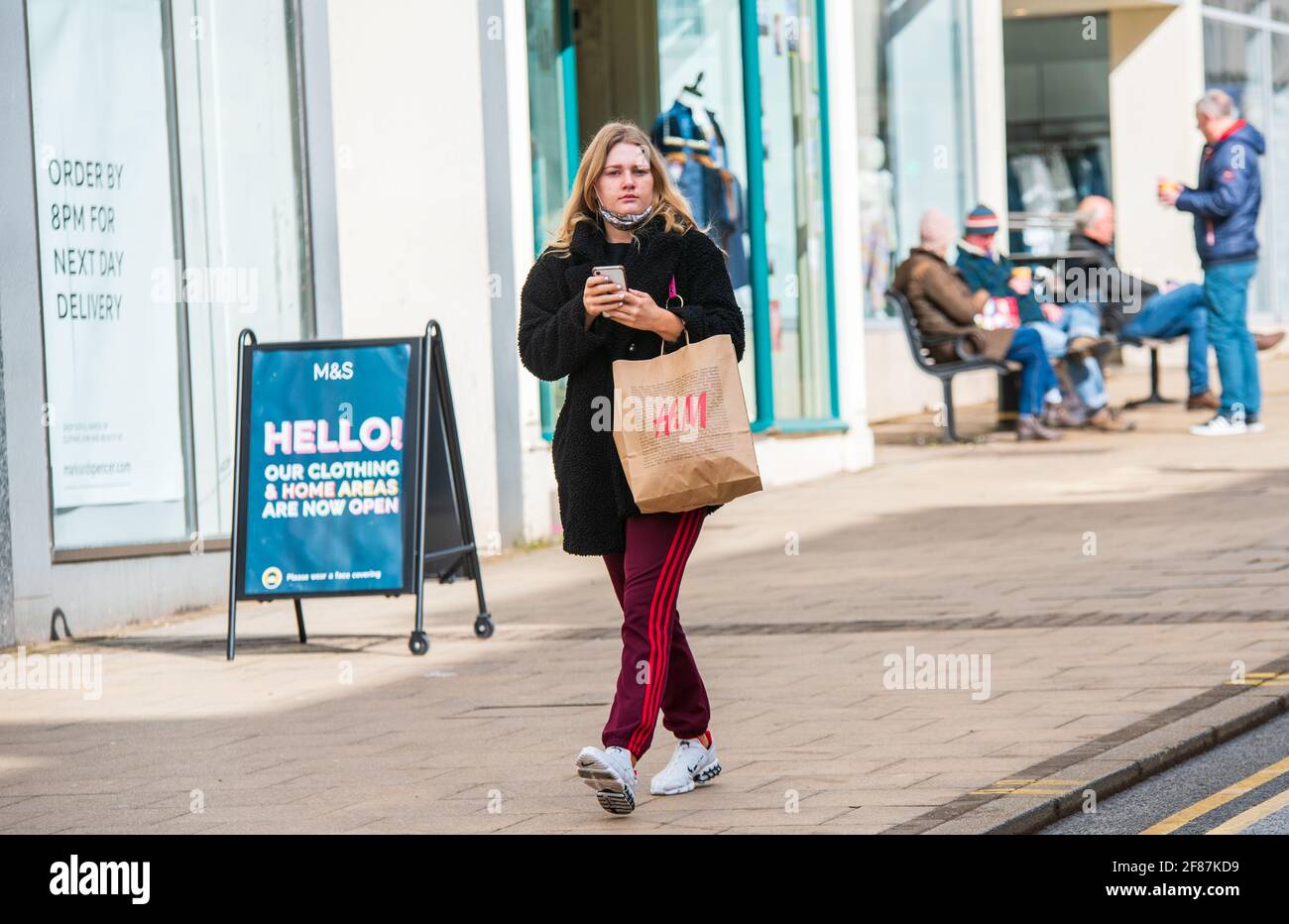 Leamington Spa, 12th April 2021: A woman walks down The Parade with an H&M  shopping bag, as non-retail stores, including clothes shop and hairdressers  reopen. Credit: Ryan Underwood / Alamy Live News