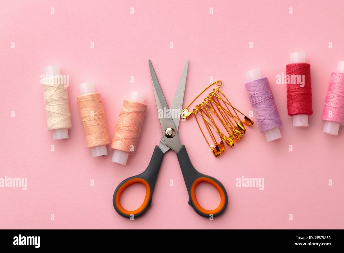 Sewing accessories including thread spools and pins on pink background Stock Photo