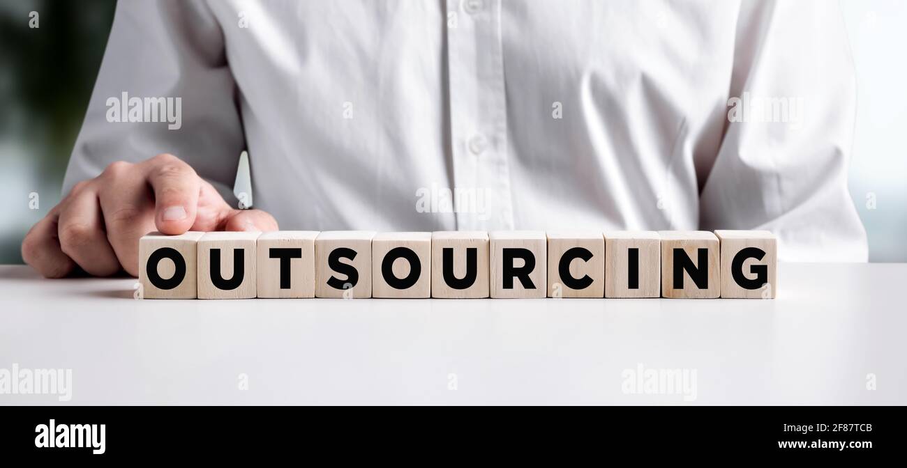 Businessman pressing his finger on the wooden cubes with the word outsourcing. Business concept. Stock Photo