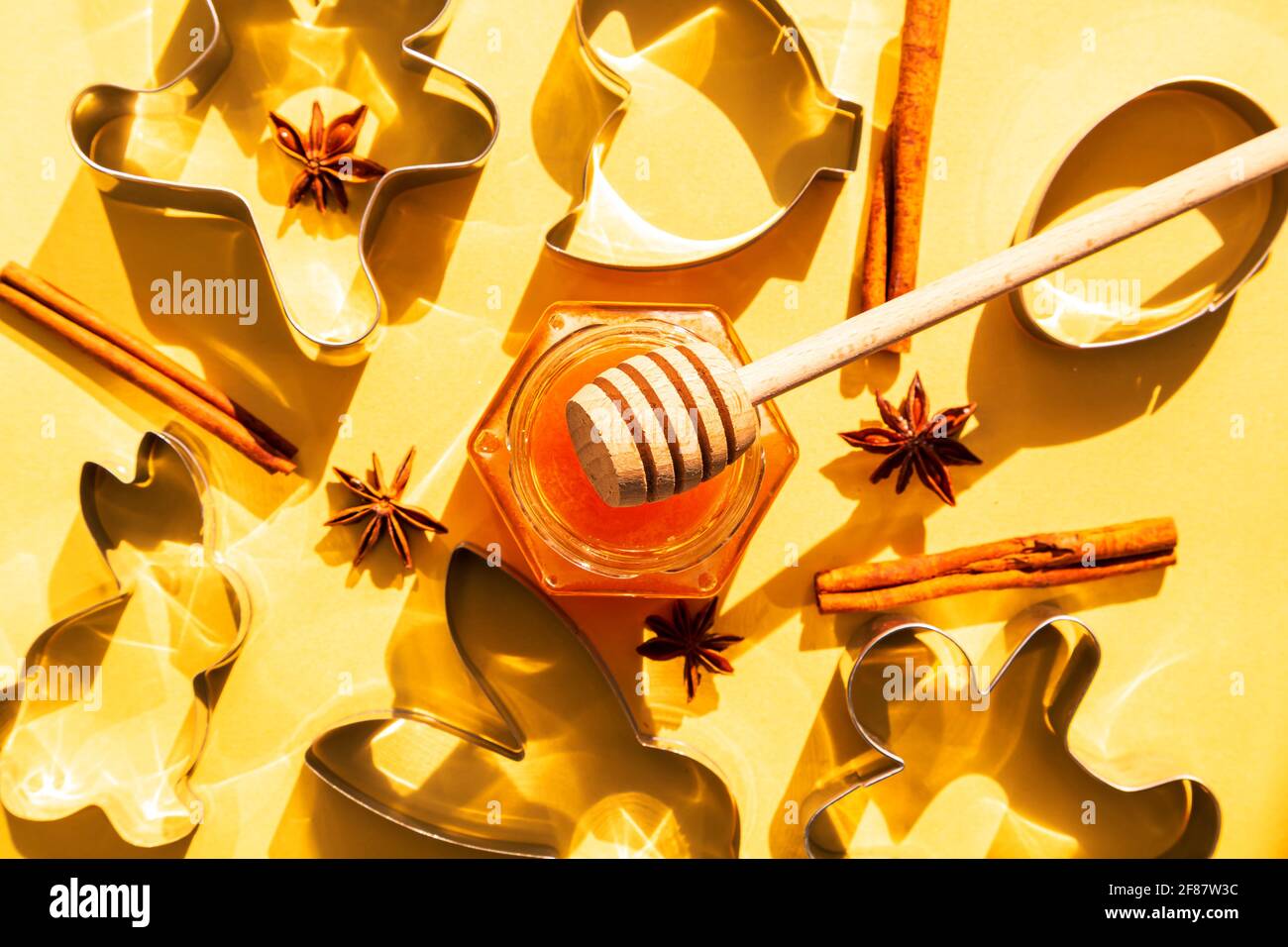 Honey jar, honey dipper and cookie cutters on yellow background. Preparing to bake cookies. Bright sunshine Stock Photo