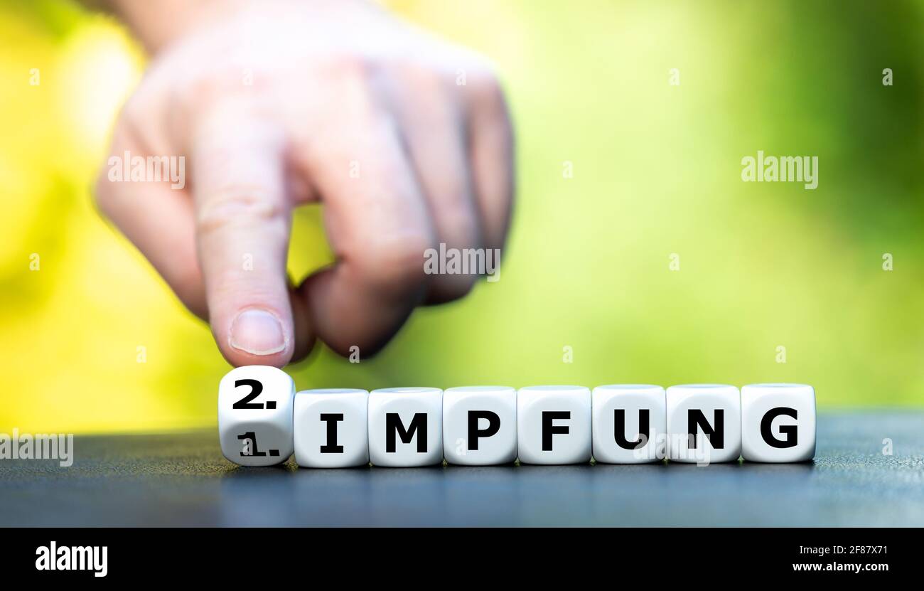 Symbol for the second vaccination dose. Hand turns dice and changes the German expression "1. Impfung" (1st dose) to "2. Impfung" (2nd dose). Stock Photo