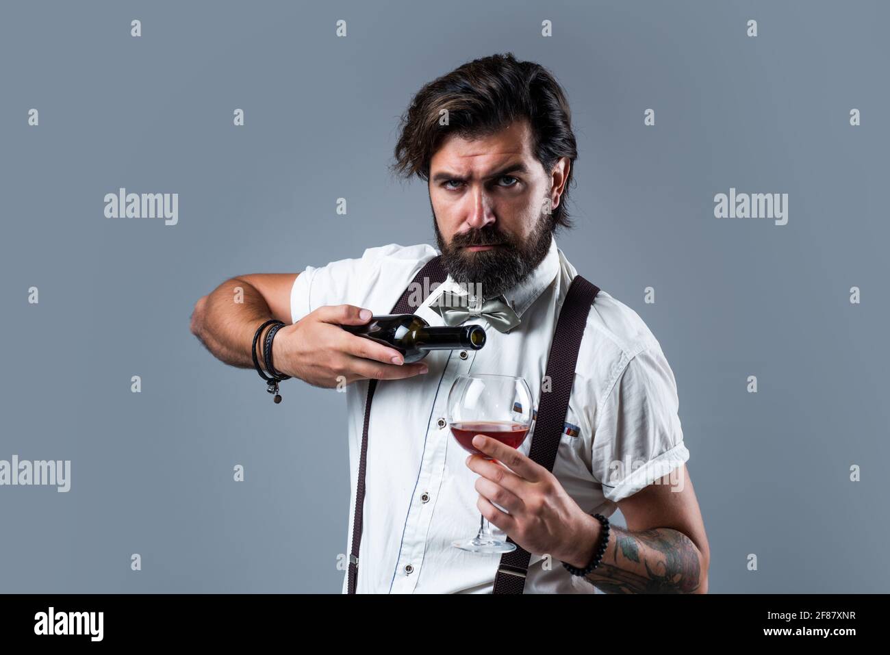 brutal bearded male with stylish look drink wine, barkeeper Stock Photo