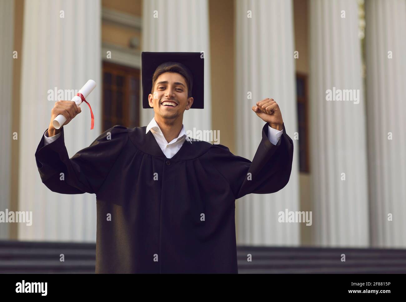 Happy university graduate standing with diploma in hand and expressing ...