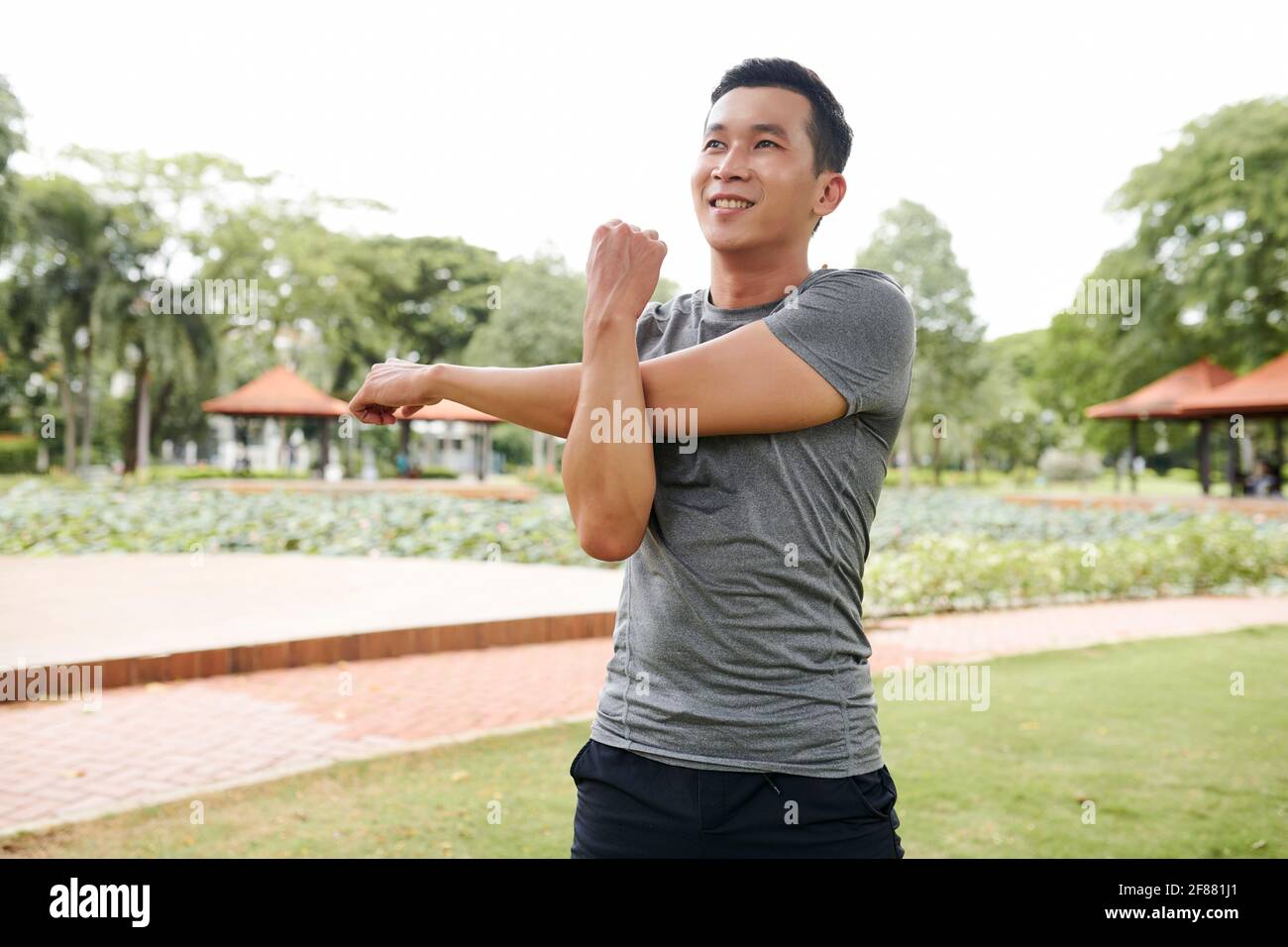 Portrait of handsome fit young Asian man stretching arms and warming up after jogging outdoors Stock Photo