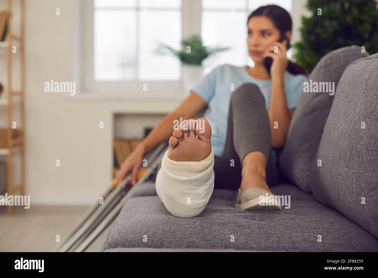 Woman with broken leg in cast lying relaxing on sofa with crutches nearby  and talking on phone Stock Photo - Alamy