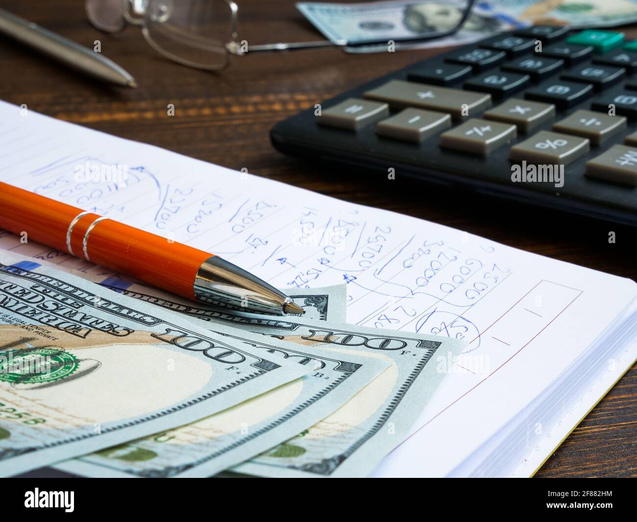 Financial calculations written by hand in a notebook, dollars and a calculator. Stock Photo