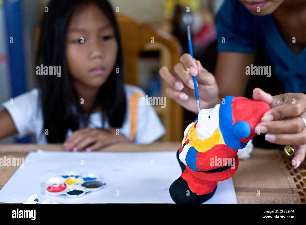 Child painting ceramic figure with help and guidance from her mother Stock Photo
