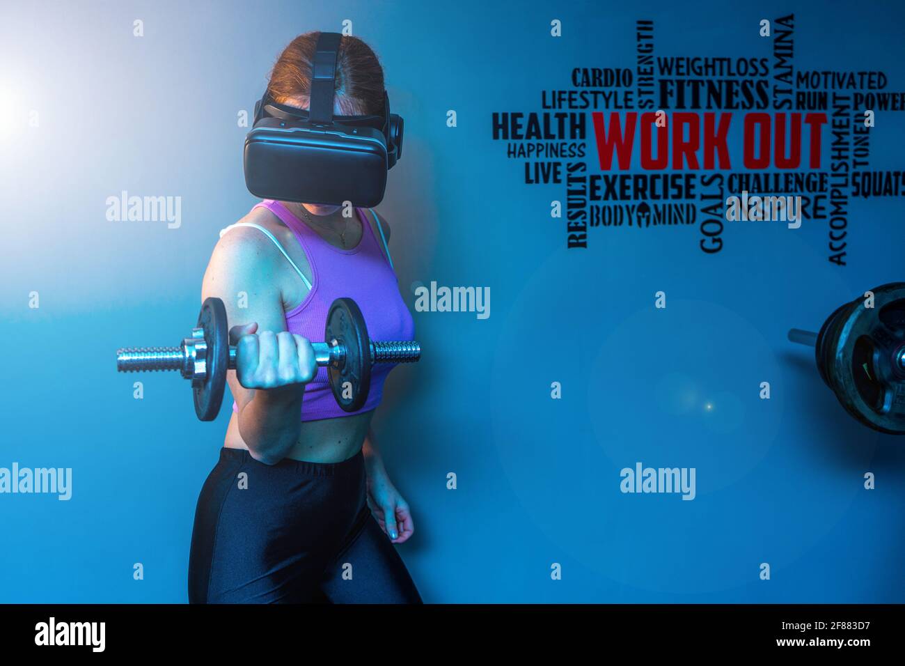 Attractive young red hair sportswoman training biceps in the gym of her beautiful house with vr futuristic goggles - Ginger athletic model Stock Photo