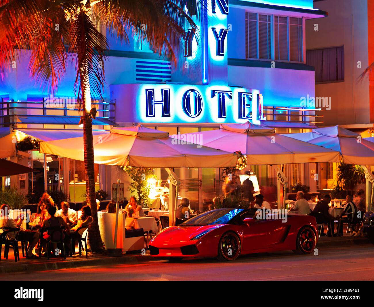 USA,Florida, South Beach Miami, Neon signs, art deco hotel and restaurants illuminated at night on Ocean Drive. Red sports car parked . Stock Photo