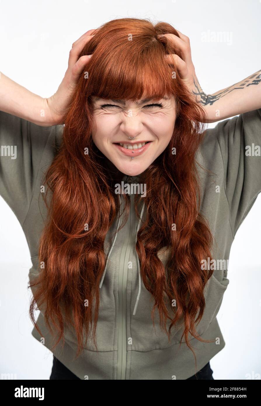 Portrait of a woman with red hair infront of white background with stressed expression pulling hair out Stock Photo