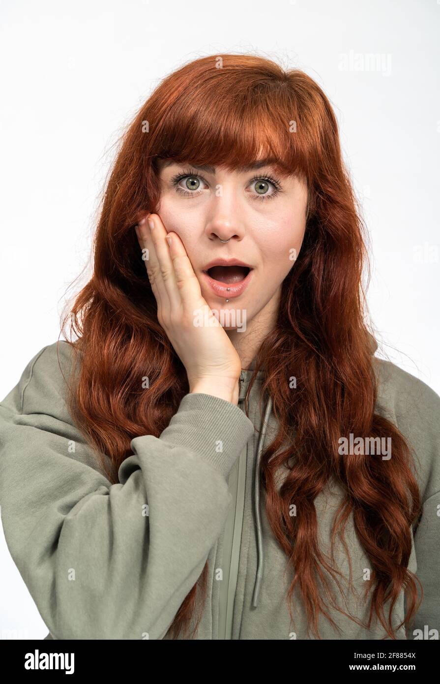 Portrait of a woman with red hair infront of white background looking surprised into camera Stock Photo