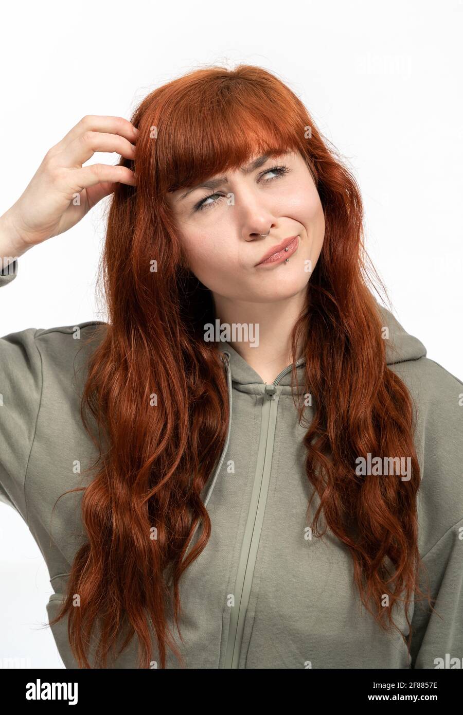 Portrait of a woman with red hair infront of white background making faces and scratching head Stock Photo