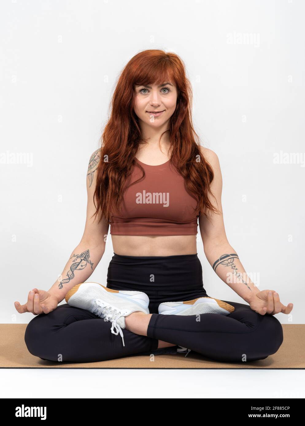 Portrait of a woman with red hair infront of white background in tailor seat folding hands Stock Photo